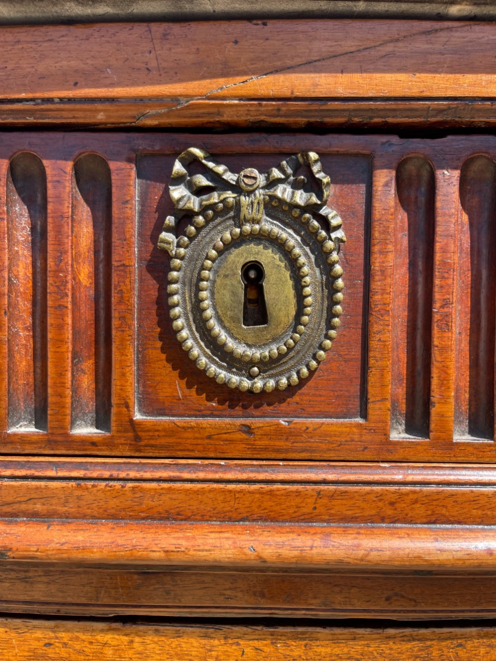 An 18th-century French cherrywood commode featuring a dark grey marble top, three frieze drawers above two long drawers, fluted sides, brass ring handles, and tapered legs. View X