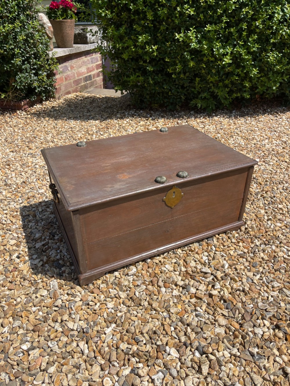 A late eighteenth-century rectangular warm brown teak trunk with a brass keyhole escutcheon, ribbed metal bosses on the lid, and metal side carrying handles.