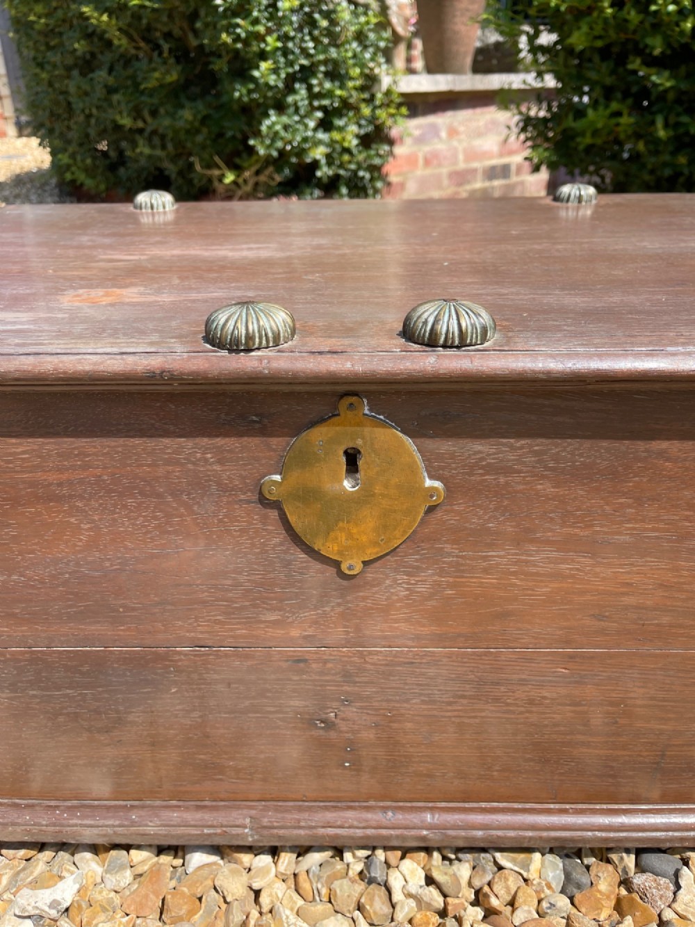 A late eighteenth-century rectangular warm brown teak trunk with a brass keyhole escutcheon, ribbed metal bosses on the lid, and metal side carrying handles. View VI