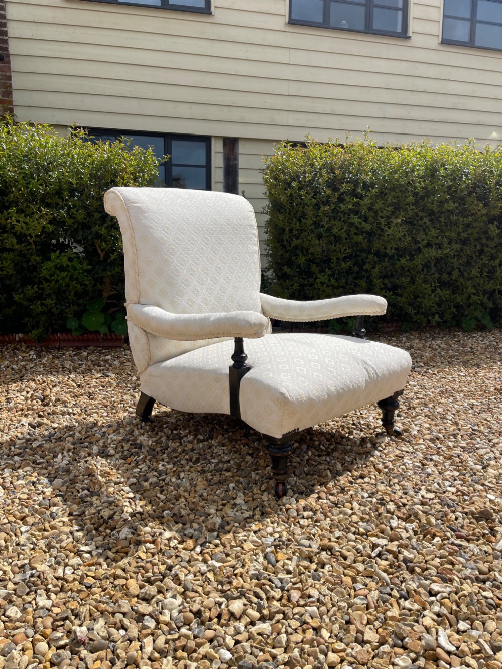 A Victorian open armchair upholstered in cream damask pattern fabric featuring turned dark wood arm supports and front legs with castors.