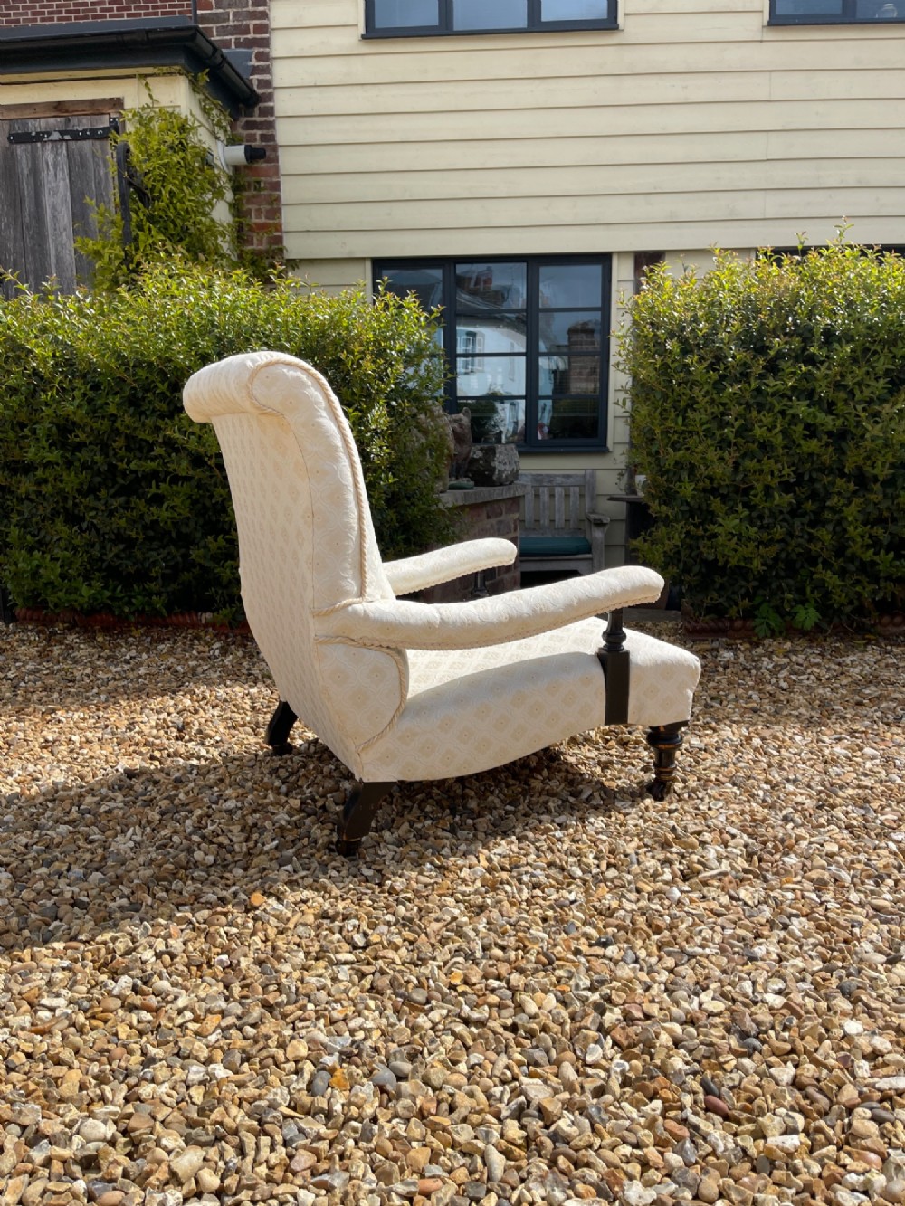 A Victorian open armchair upholstered in cream damask pattern fabric featuring turned dark wood arm supports and front legs with castors. View II