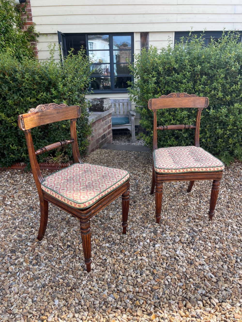 A pair of antique Regency side chairs featuring carved top rails, reeded front legs, and patterned upholstered drop-in seats.