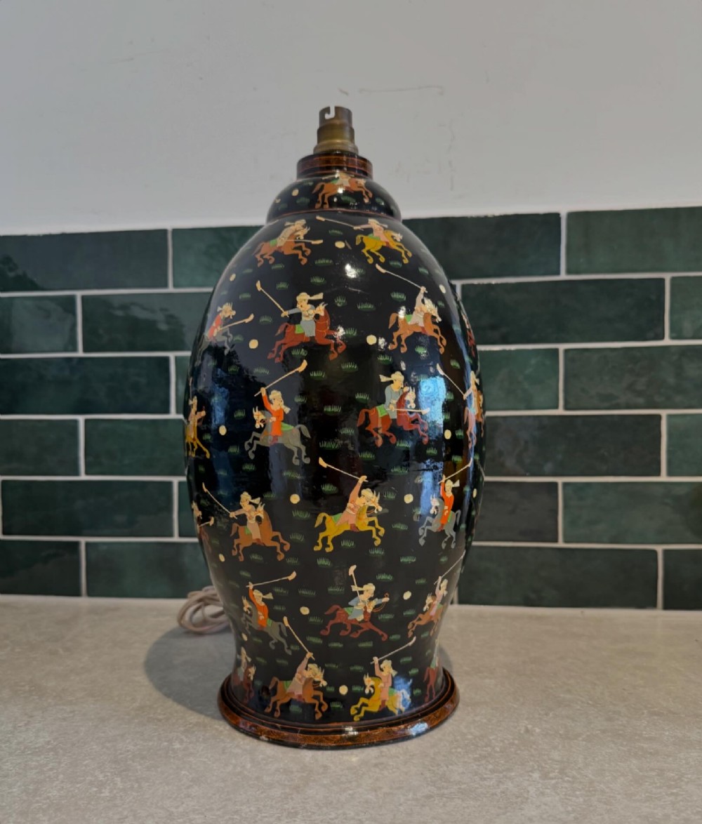 A hand-painted black papier-mache table lamp base depicting figures on horseback playing polo.