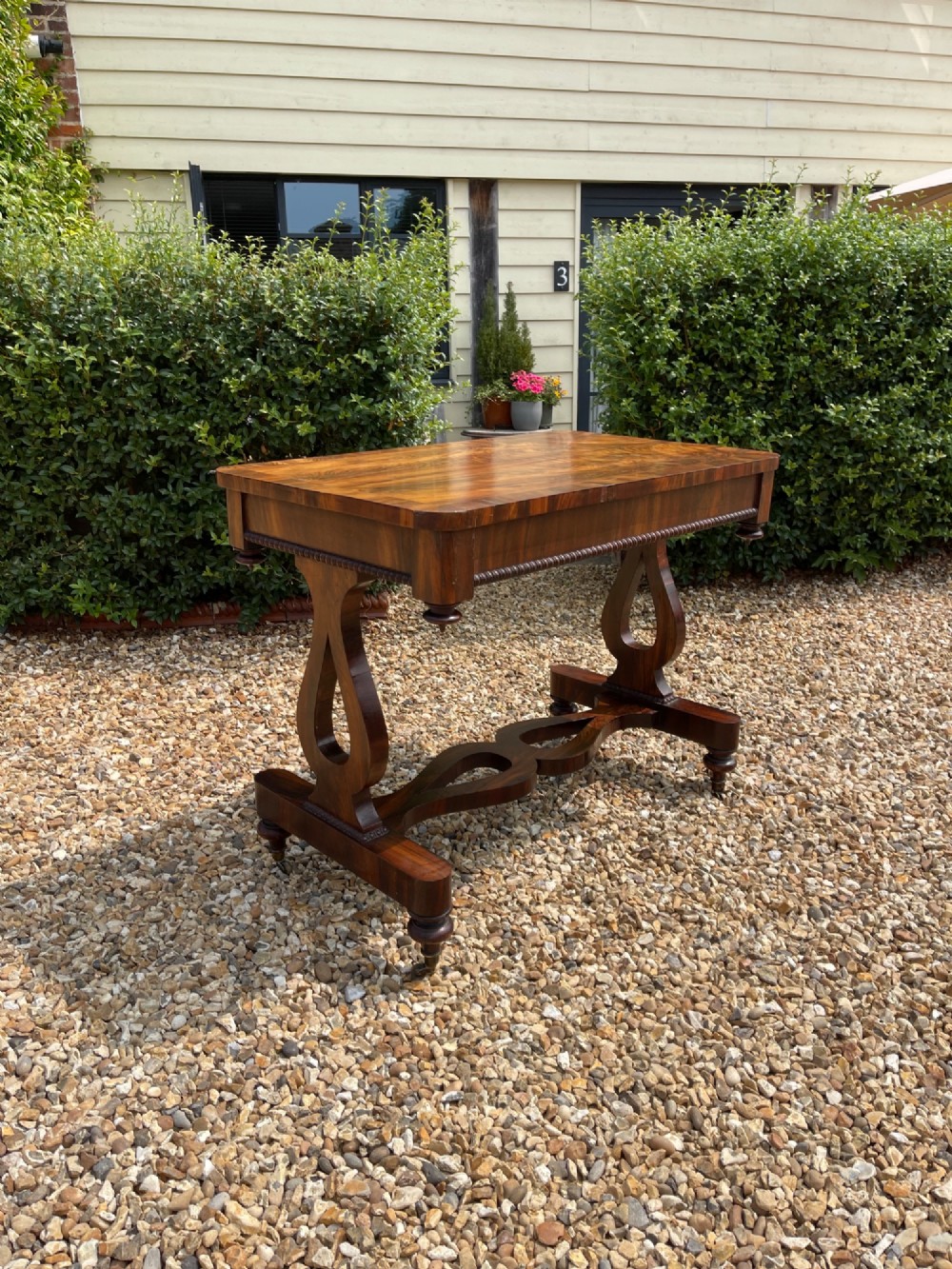 A 19th-century dark wood library table featuring lyre-shaped side supports, a carved central stretcher, beaded moulding, and brass castors.