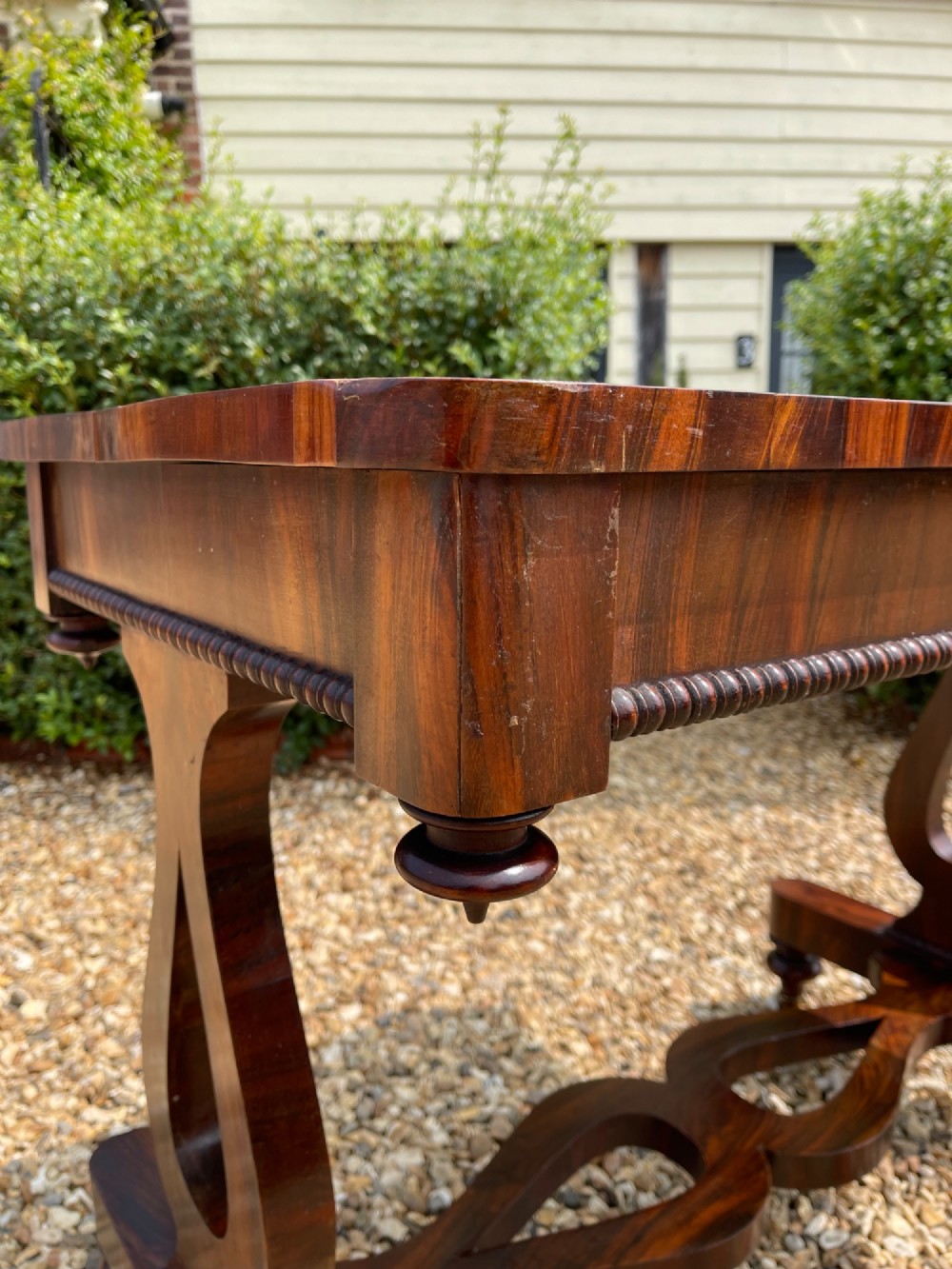A 19th-century dark wood library table featuring lyre-shaped side supports, a carved central stretcher, beaded moulding, and brass castors. View II