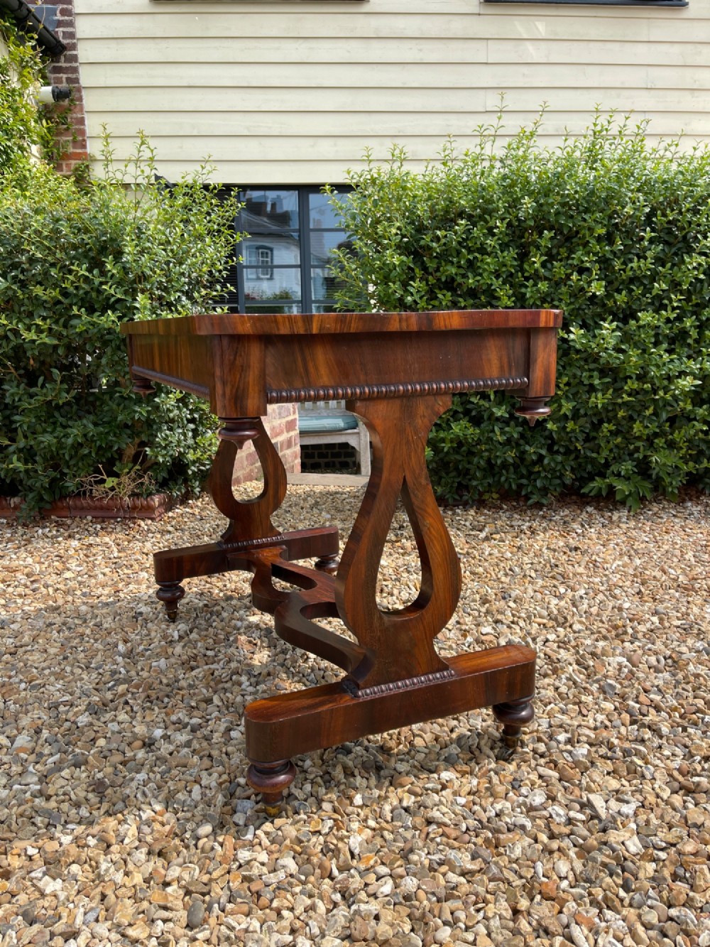 A 19th-century dark wood library table featuring lyre-shaped side supports, a carved central stretcher, beaded moulding, and brass castors. View VI