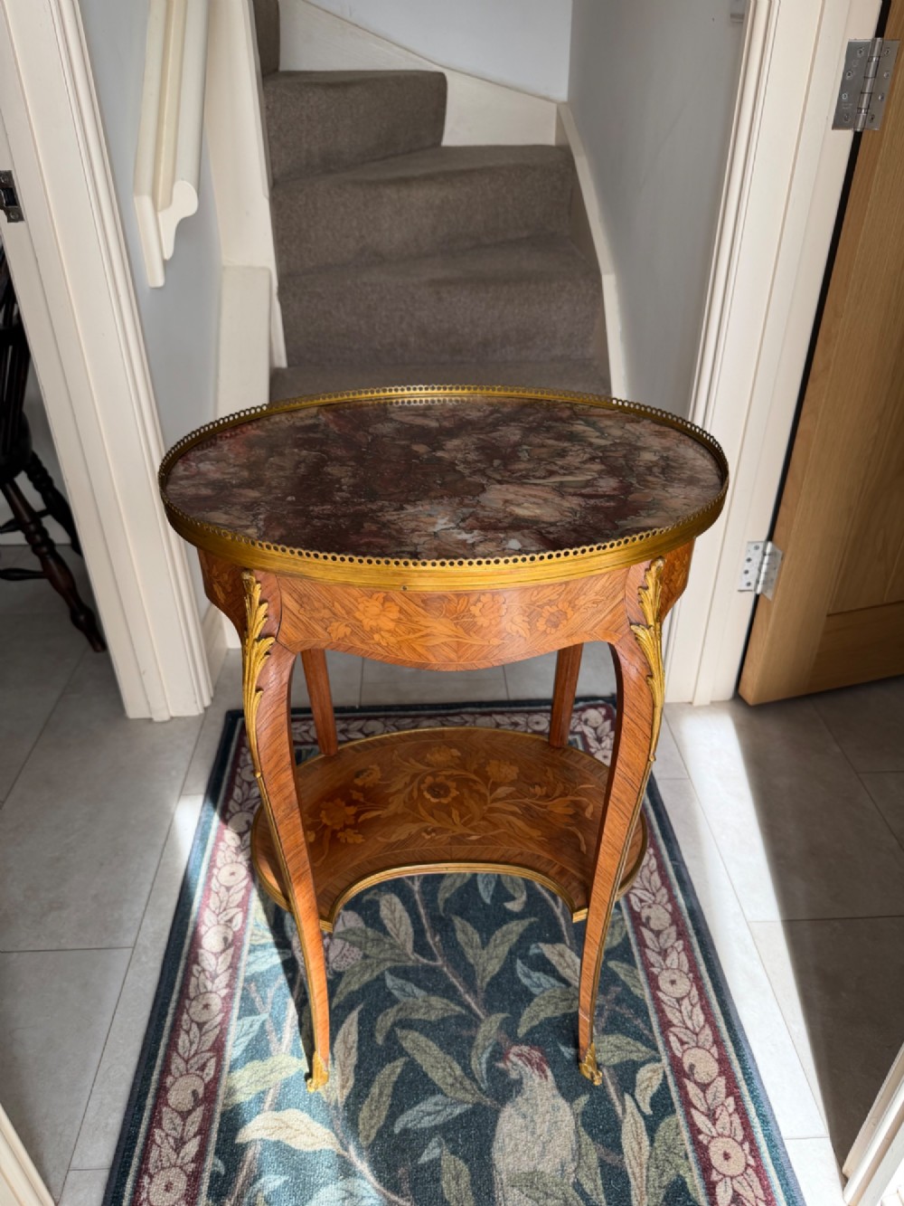 An oval French Louis XV style kingwood side table featuring a mottled red marble top, pierced brass gallery, floral marquetry inlay, and cabriole legs with bronze mounts.