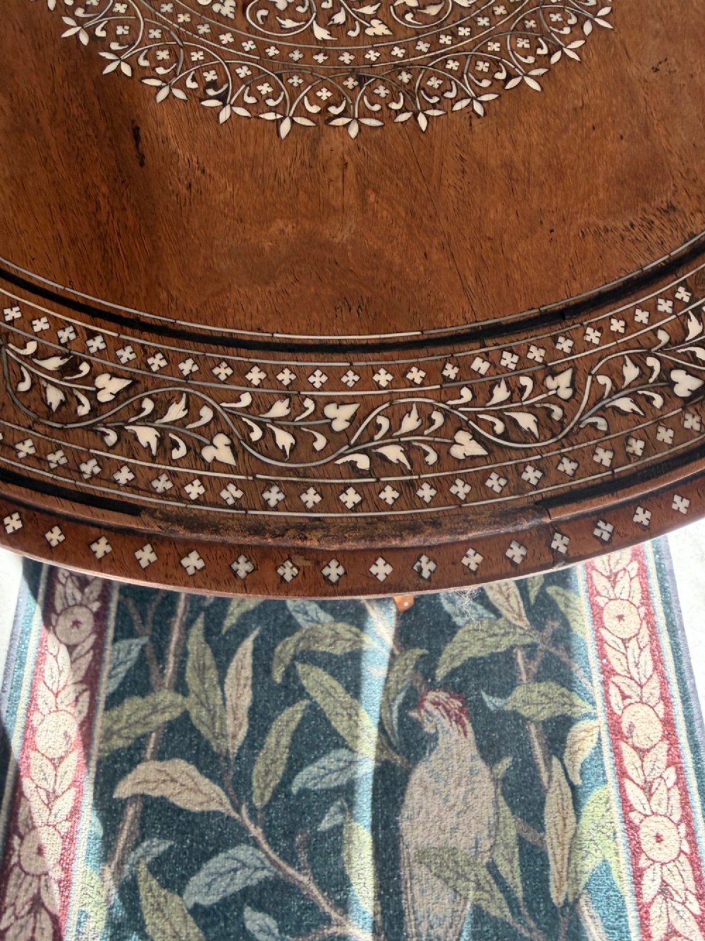 A circular dark wood Anglo-Indian pedestal table featuring intricate bone inlay patterns across the tabletop, turned central column, and tripod feet. View III