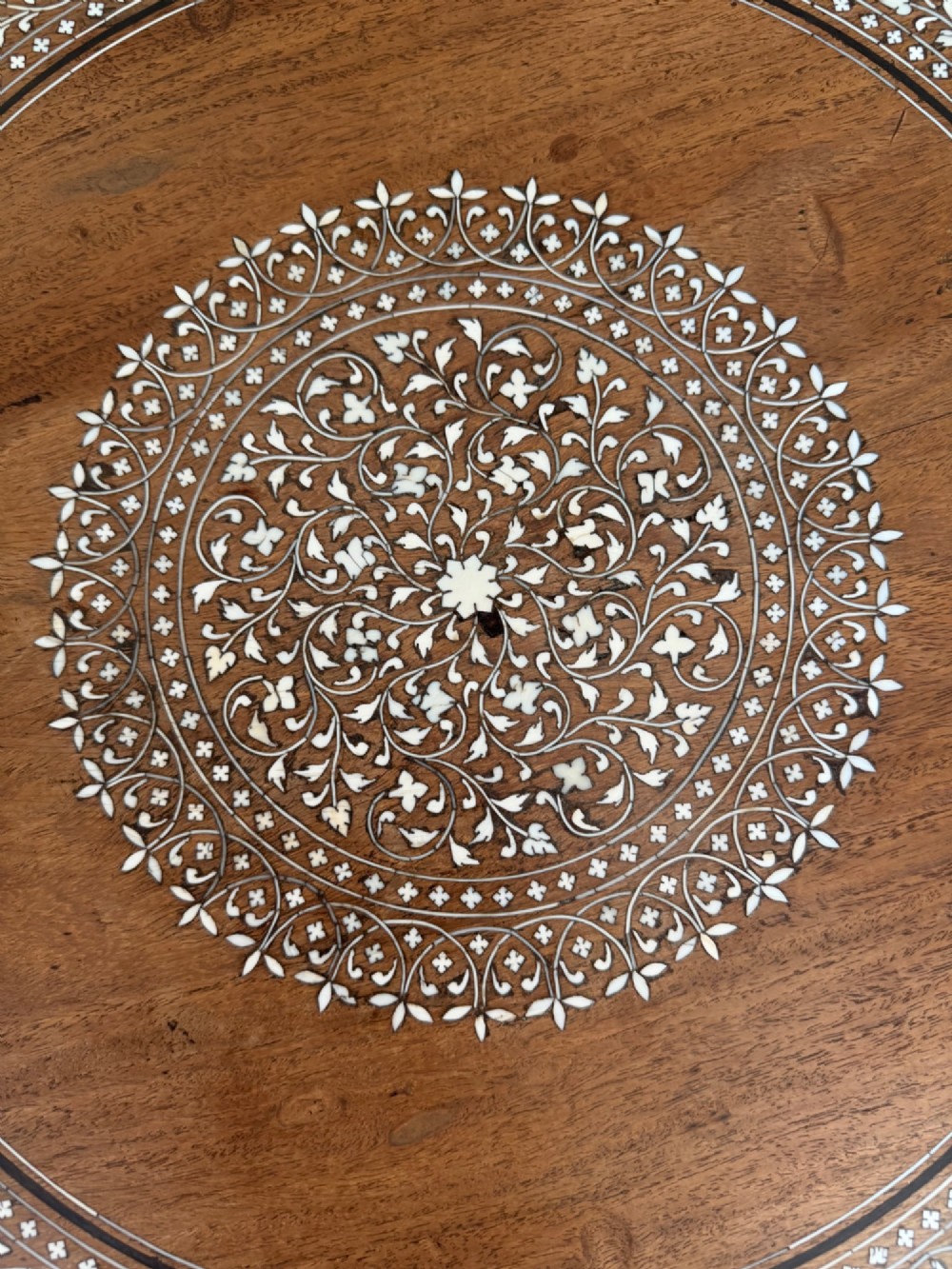 A circular dark wood Anglo-Indian pedestal table featuring intricate bone inlay patterns across the tabletop, turned central column, and tripod feet. View IV