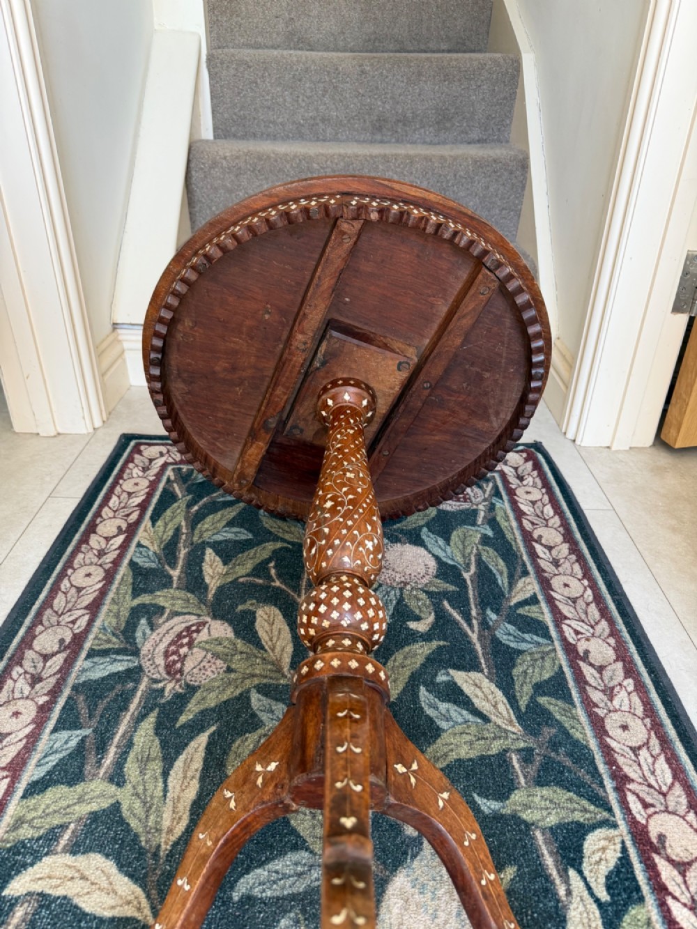 A circular dark wood Anglo-Indian pedestal table featuring intricate bone inlay patterns across the tabletop, turned central column, and tripod feet. View V