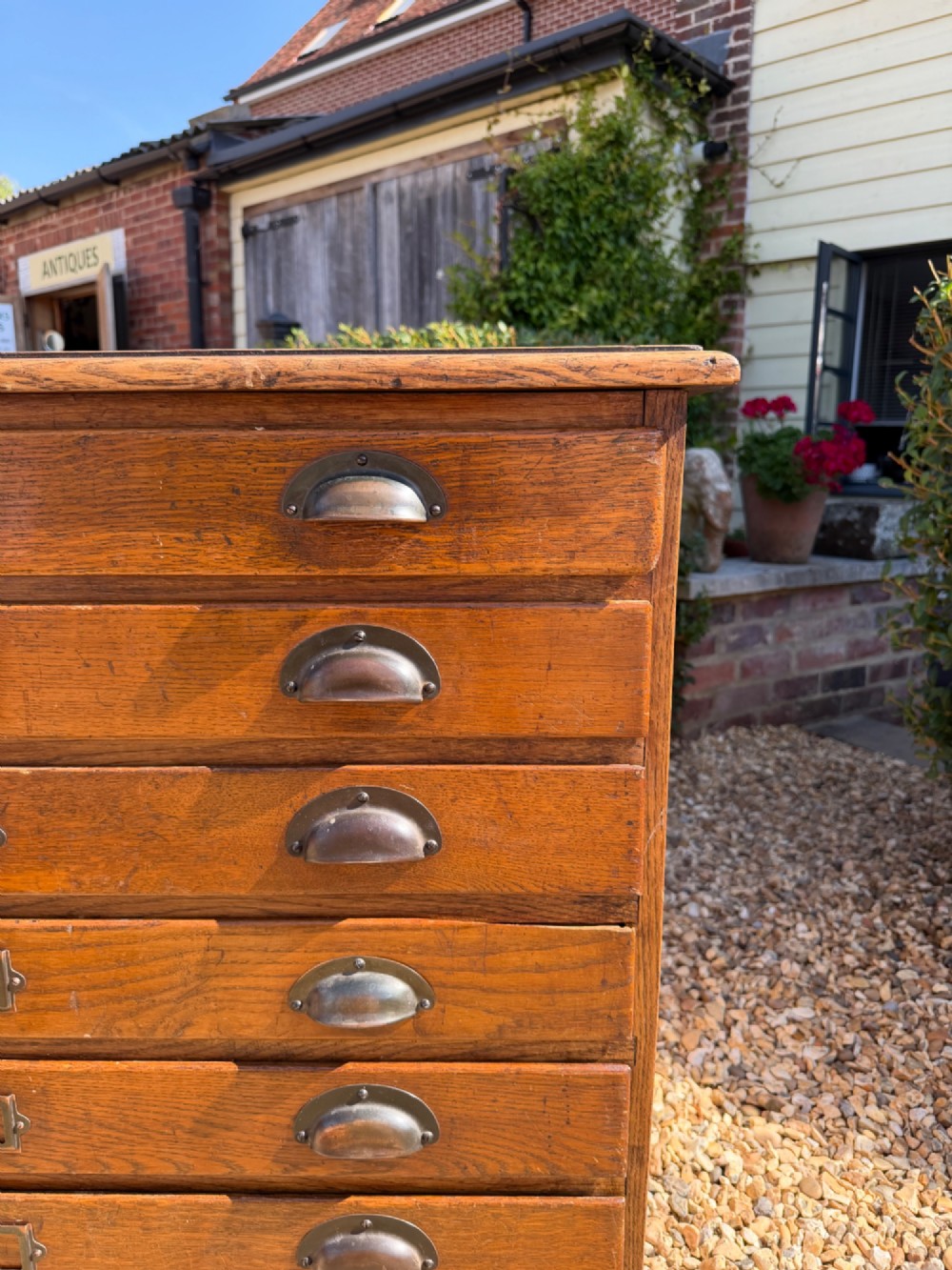 A seven-drawer antique oak plan chest featuring shell cup handles and central metal index label holders on each wide shallow drawer front. View V