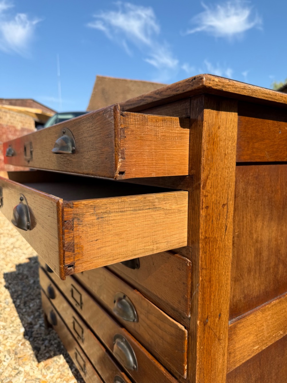 A seven-drawer antique oak plan chest featuring shell cup handles and central metal index label holders on each wide shallow drawer front. View VI