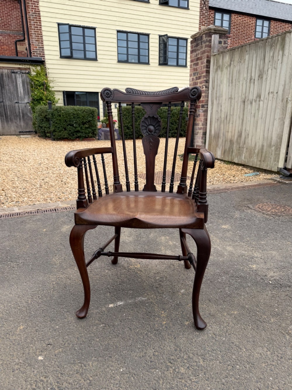 A carved dark mahogany armchair featuring cabriole front legs, turned spindles, a central shell back splat, and a shaped wooden seat.