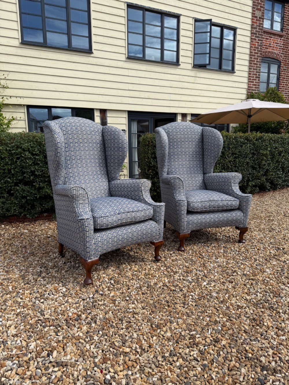 A pair of high-backed wingback armchairs upholstered in blue and grey geometric patterned fabric with carved dark timber cabriole legs.