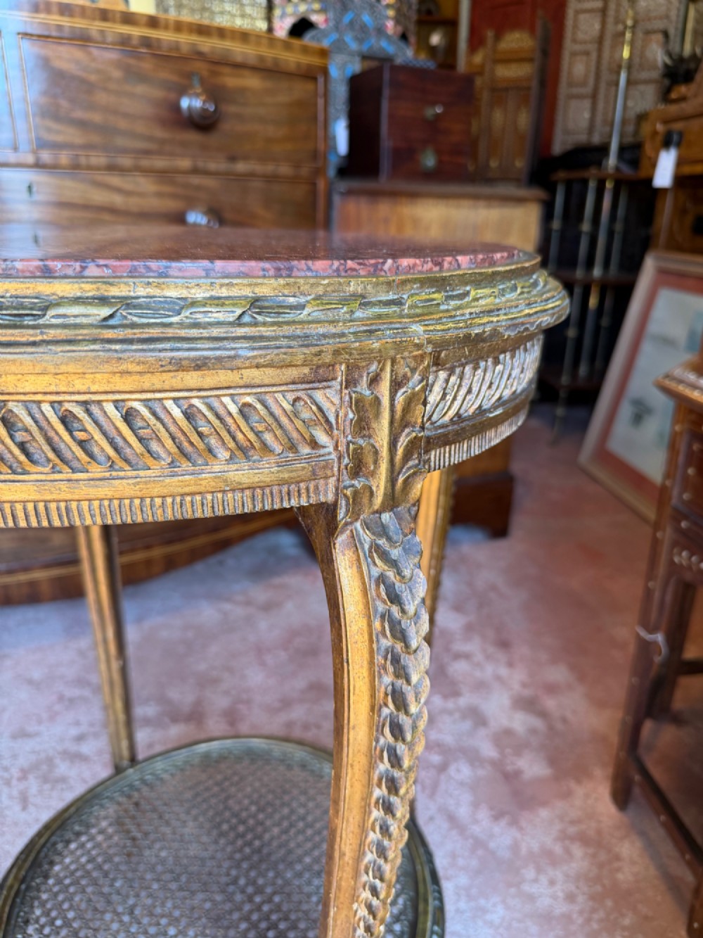 A nineteenth-century French circular gueridon table featuring a red marble top, carved giltwood frame, and lower caned tier. View II