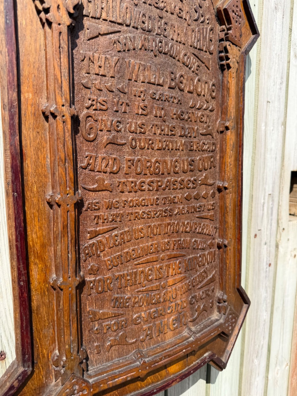 A vertical carved dark oak plaque shaped like a Gothic arch with a cross finial, featuring relief-carved lettering of the Lords Prayer. View III