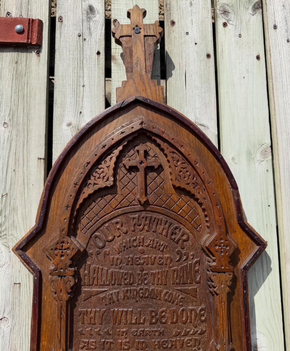 A vertical carved dark oak plaque shaped like a Gothic arch with a cross finial, featuring relief-carved lettering of the Lords Prayer. View V