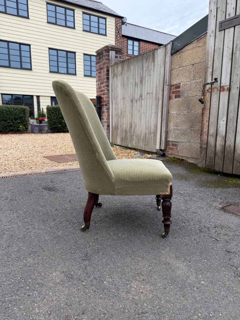 An antique George IV slipper chair upholstered in textured sage green fabric with carved mahogany front legs featuring brass castors. View II