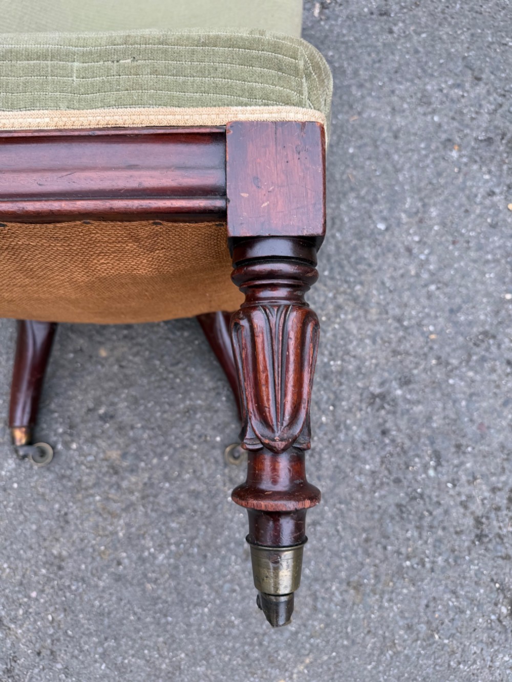 An antique George IV slipper chair upholstered in textured sage green fabric with carved mahogany front legs featuring brass castors. View III