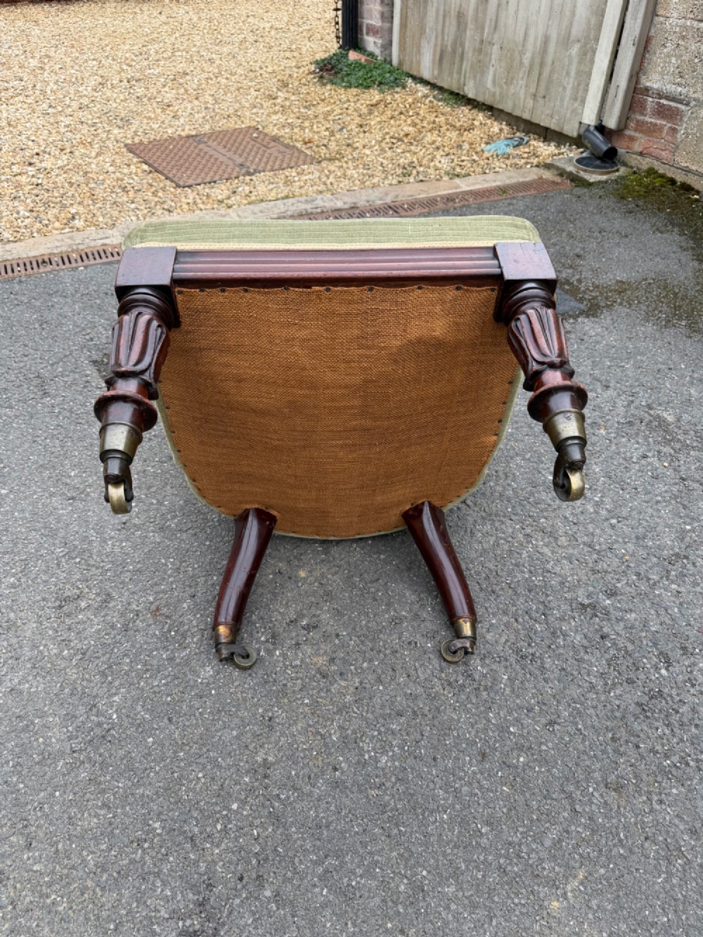 An antique George IV slipper chair upholstered in textured sage green fabric with carved mahogany front legs featuring brass castors. View V