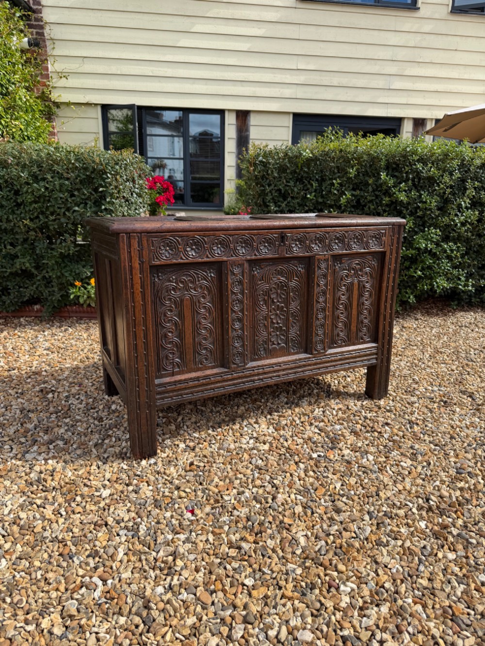 A 17th-century dark oak coffer featuring three carved panelled sections on the front, rosette border carvings, and peg joinery.