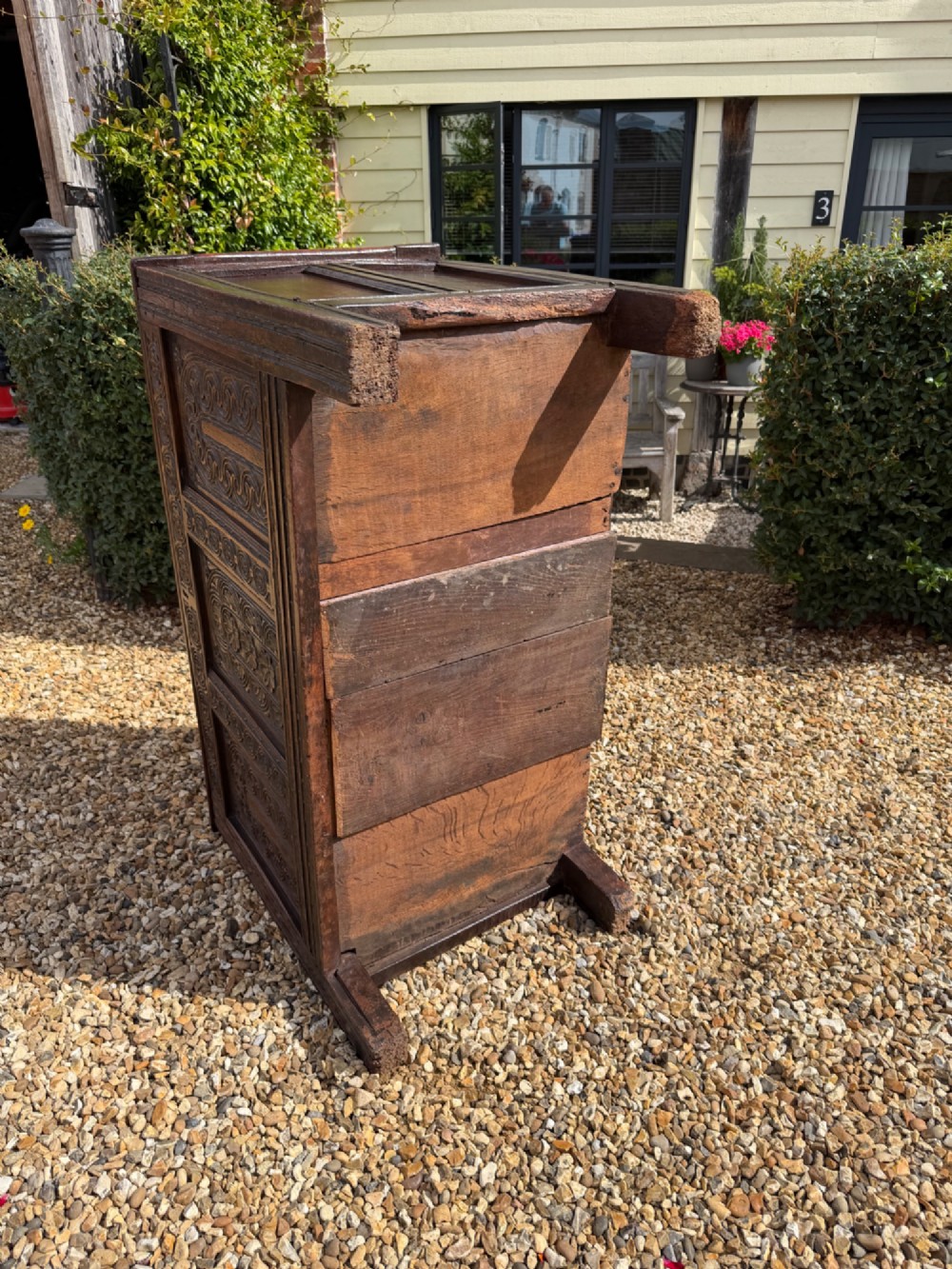 A 17th-century dark oak coffer featuring three carved panelled sections on the front, rosette border carvings, and peg joinery. View V