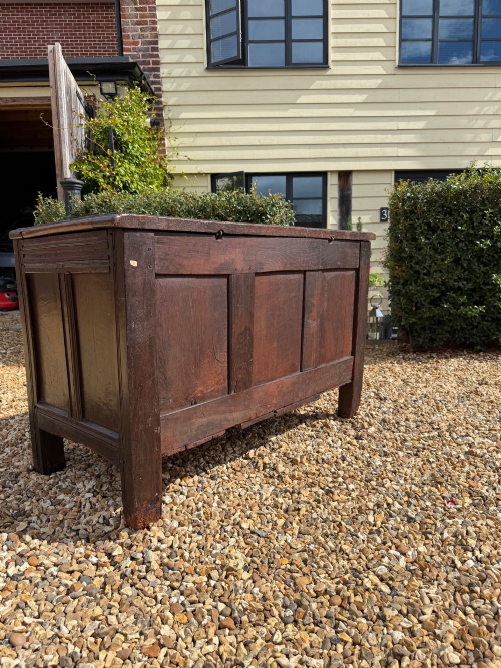 A 17th-century dark oak coffer featuring three carved panelled sections on the front, rosette border carvings, and peg joinery. View VI