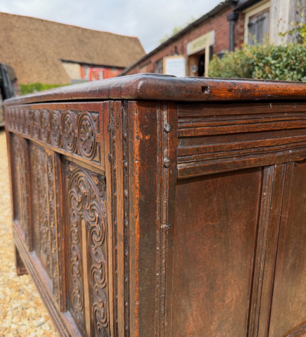 A 17th-century dark oak coffer featuring three carved panelled sections on the front, rosette border carvings, and peg joinery. View VIII