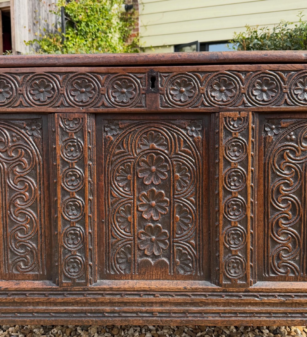 A 17th-century dark oak coffer featuring three carved panelled sections on the front, rosette border carvings, and peg joinery. View IX