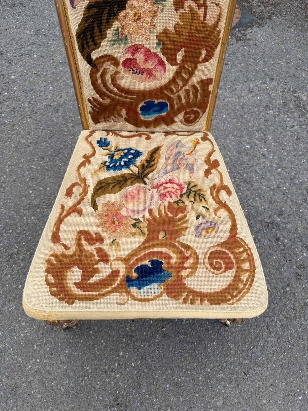A nineteenth-century prie dieu chair featuring floral needlepoint upholstery, a low seat, a tall T-shaped backrest, and fluted giltwood legs on brass castors. View II