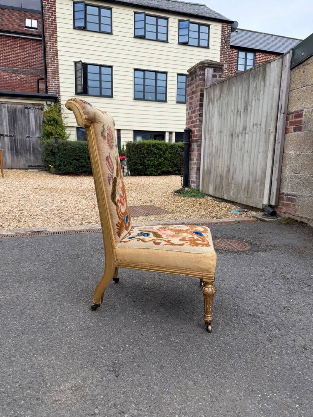A nineteenth-century prie dieu chair featuring floral needlepoint upholstery, a low seat, a tall T-shaped backrest, and fluted giltwood legs on brass castors. View V