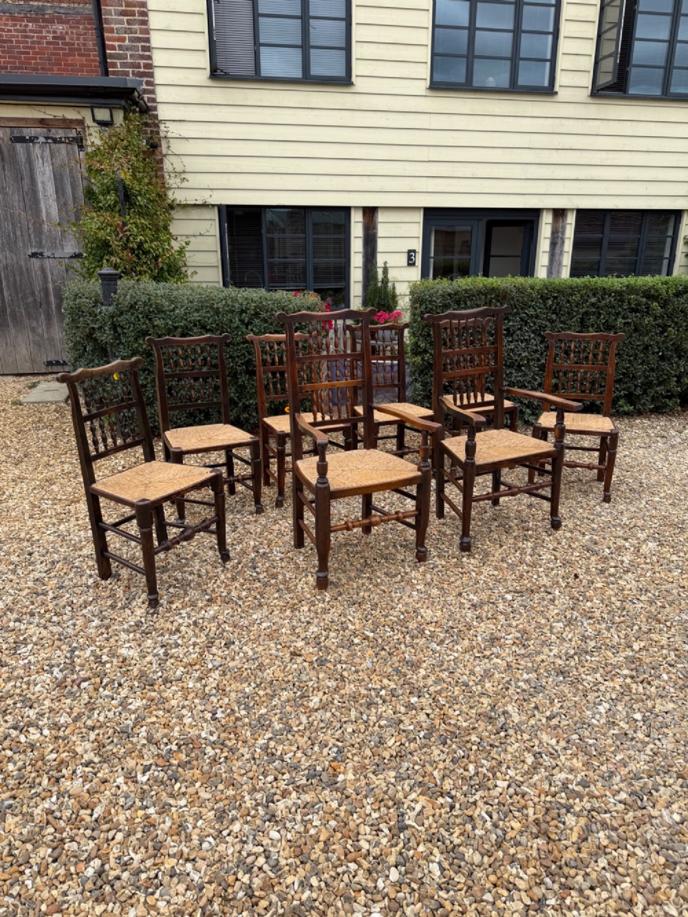 A set of eight dark wood dining chairs featuring spindle backs and woven rush seats, comprising two armchairs and six side chairs.