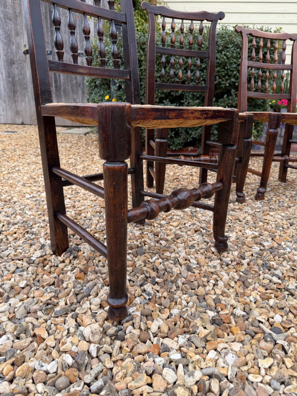 A set of eight dark wood dining chairs featuring spindle backs and woven rush seats, comprising two armchairs and six side chairs. View III