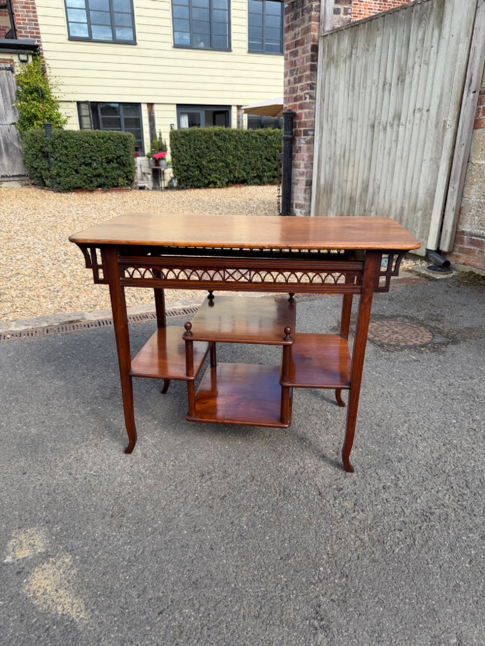 An Anglo-Japanese walnut occasional table featuring a rectangular top, an openwork fretwork frieze, and asymmetrical staggered lower shelves supported by turned spindles.