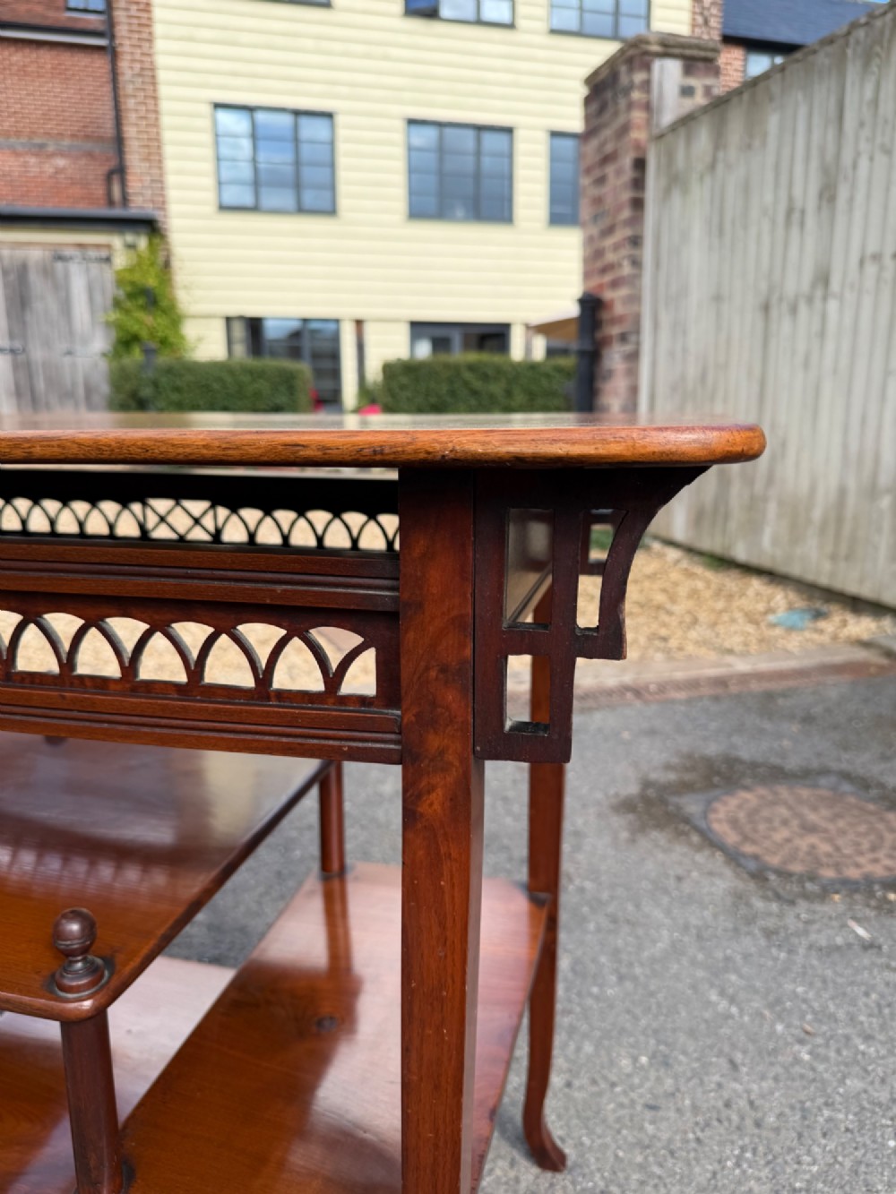 An Anglo-Japanese walnut occasional table featuring a rectangular top, an openwork fretwork frieze, and asymmetrical staggered lower shelves supported by turned spindles. View V