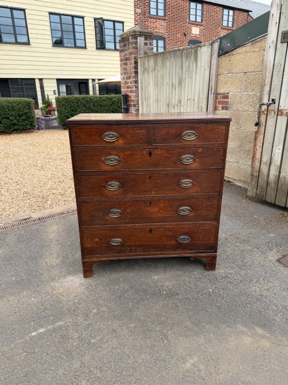 A Georgian oak chest of drawers featuring two short over three long graduated drawers with brass oval handles and bracket feet.