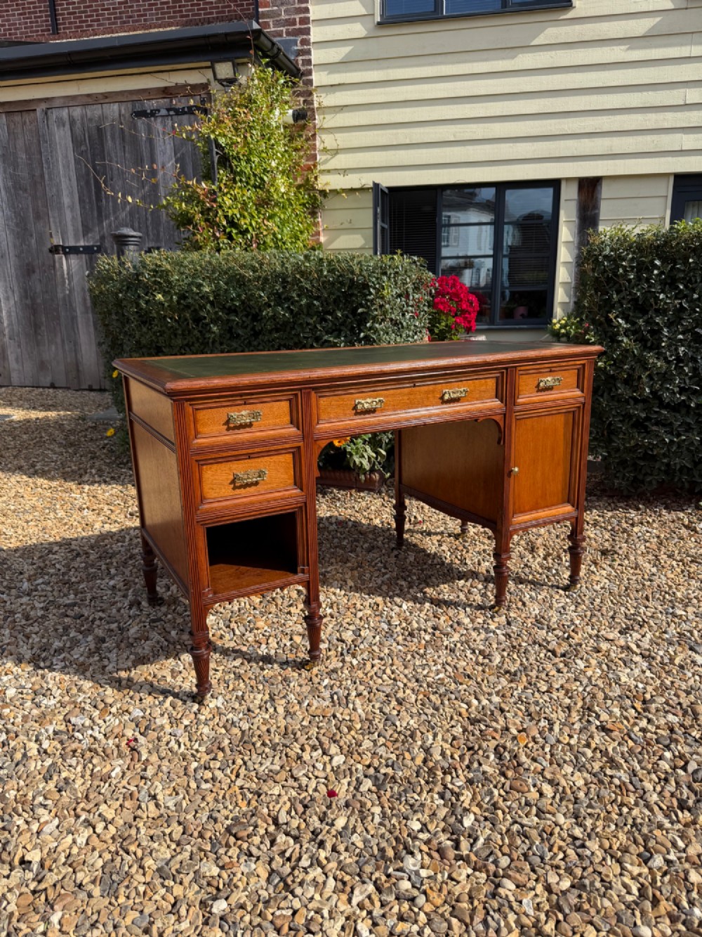 An antique walnut writing desk with a green leather inset top, brass drawer pulls, turned legs on castors, and built-in drawer pedestals.