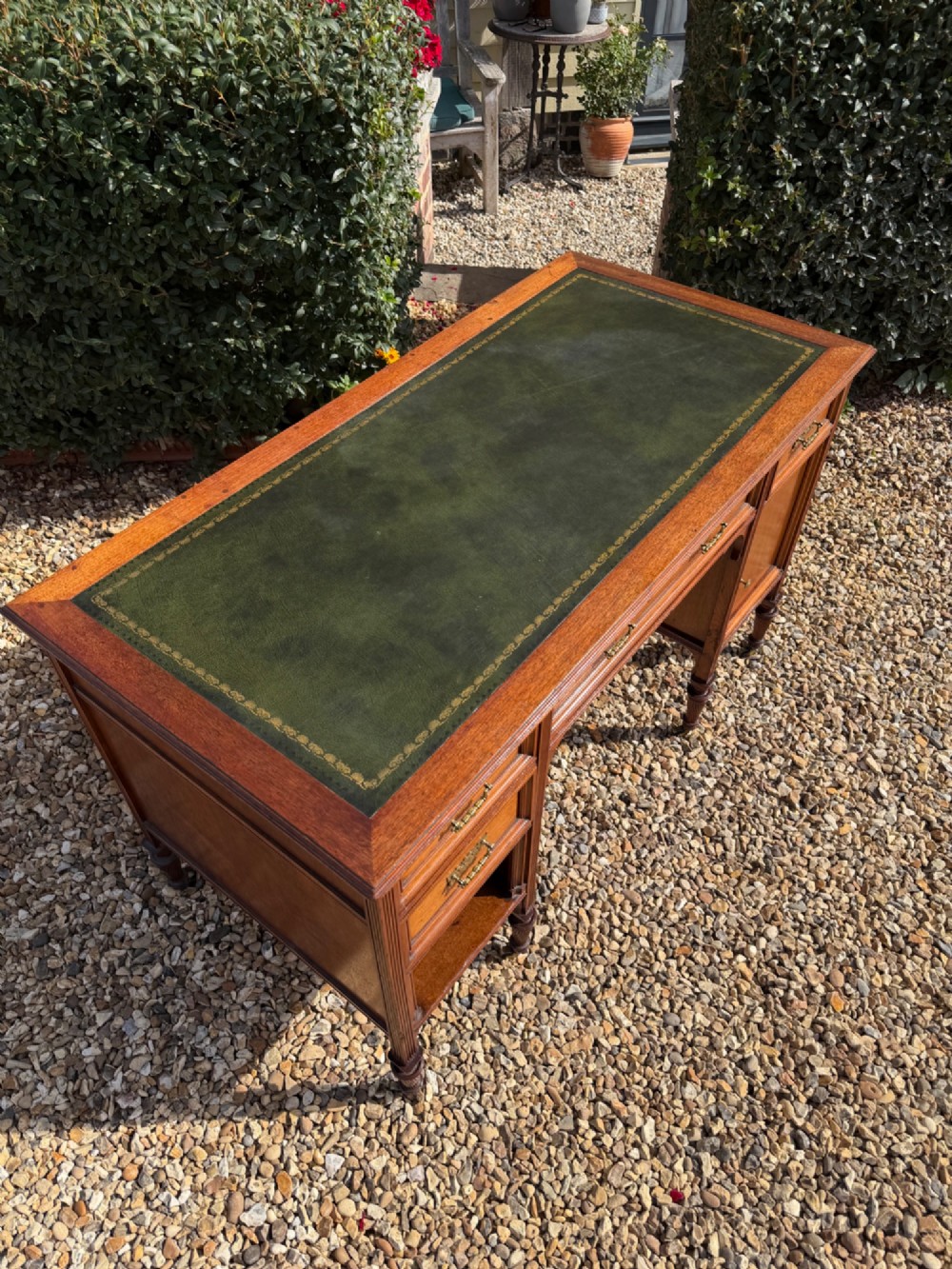 An antique walnut writing desk with a green leather inset top, brass drawer pulls, turned legs on castors, and built-in drawer pedestals. View II