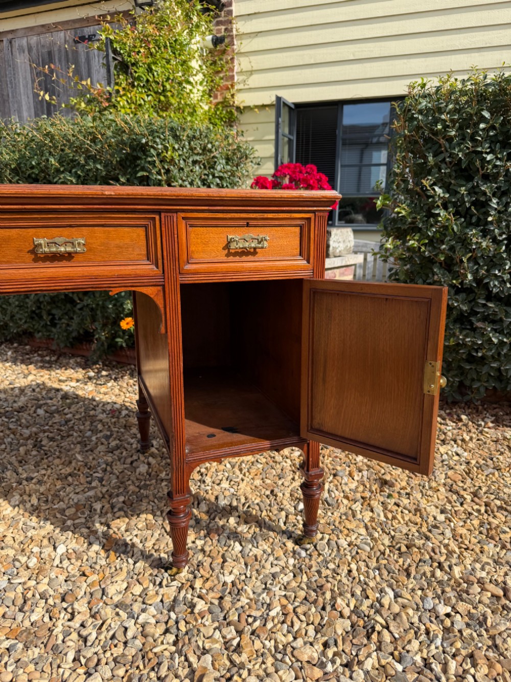 An antique walnut writing desk with a green leather inset top, brass drawer pulls, turned legs on castors, and built-in drawer pedestals. View V