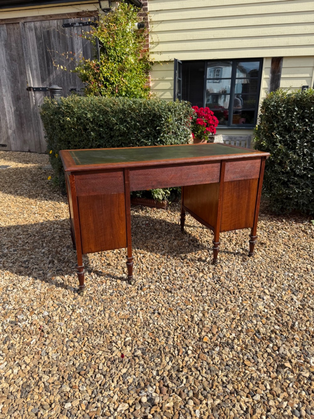 An antique walnut writing desk with a green leather inset top, brass drawer pulls, turned legs on castors, and built-in drawer pedestals. View VI