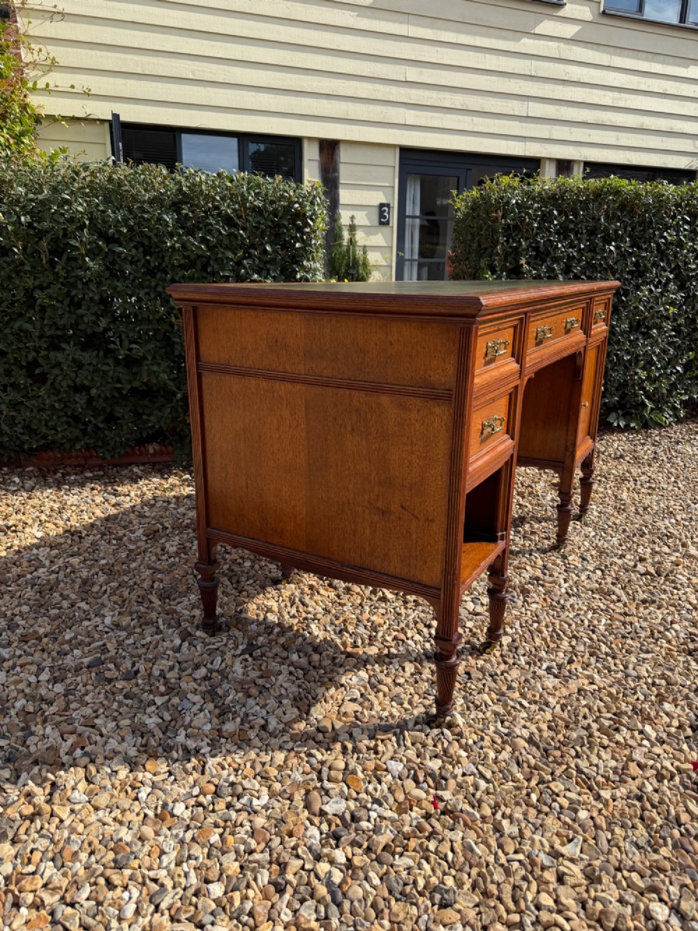 An antique walnut writing desk with a green leather inset top, brass drawer pulls, turned legs on castors, and built-in drawer pedestals. View VIII