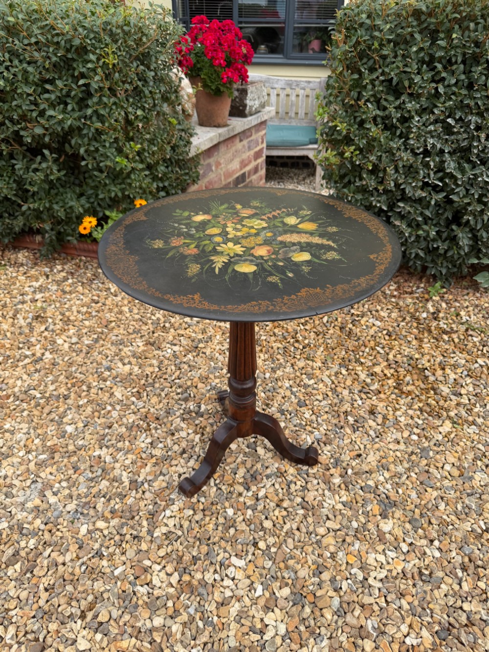 A nineteenth-century circular side table featuring a black slate top decorated with hand-painted botanical flowers and a gilt border, raised on a fluted dark wood pedestal stem with tripod legs.