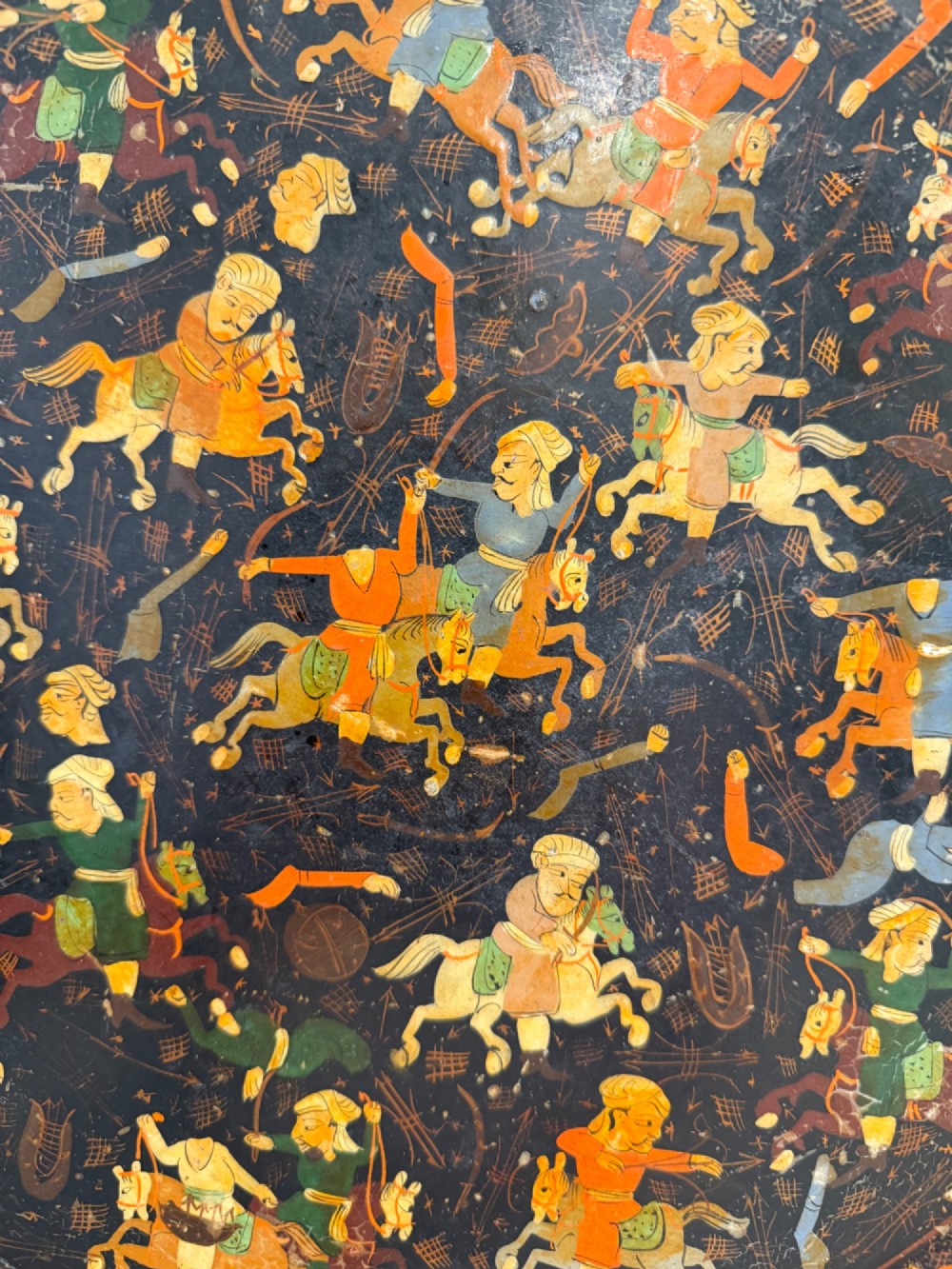 A circular black papier-mache tray hand-painted with equestrian riders in orange, green, and gold against a dark background. View II