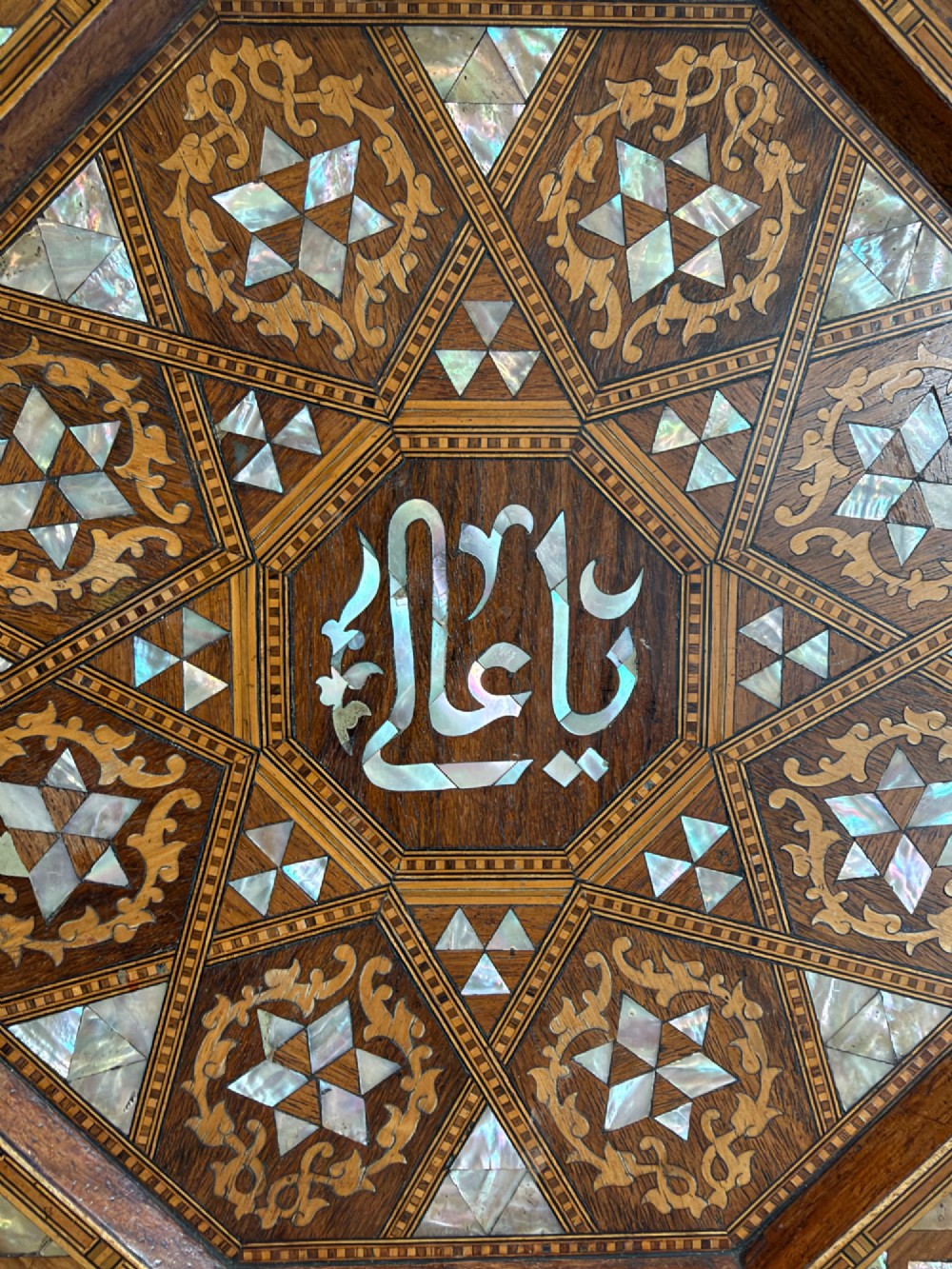 An octagonal wooden side table with intricate Moorish geometric marquetry, mother-of-pearl inlay, and Arabic calligraphy in the central medallion. View V