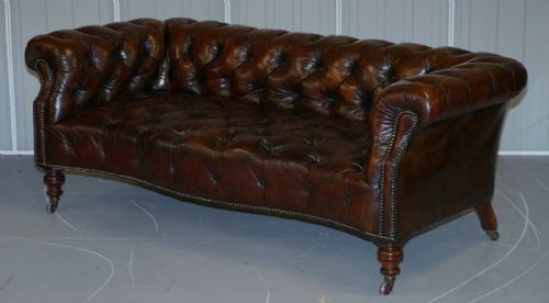 fig 1. A Victorian whisky brown leather Chesterfield sofa featuring a serpentine front, deep buttoned upholstery, brass stud detailing, and turned legs with brass castors.