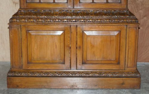 fig 3. A tall warm brown oak library bookcase featuring multi-paned glazed upper doors, intricate carved cornices, and a panelled two-door lower cabinet.