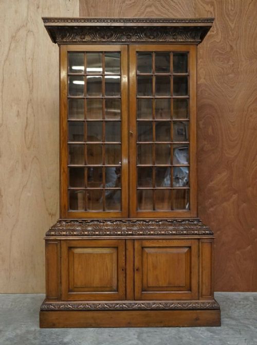 fig 5. A tall warm brown oak library bookcase featuring multi-paned glazed upper doors, intricate carved cornices, and a panelled two-door lower cabinet.
