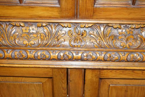 fig 6. A tall warm brown oak library bookcase featuring multi-paned glazed upper doors, intricate carved cornices, and a panelled two-door lower cabinet.