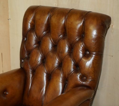 fig 3. A William IV brown leather Chesterfield armchair featuring deep buttoning, brass studding, turned legs on castors, and an attached swivel mahogany writing slope.