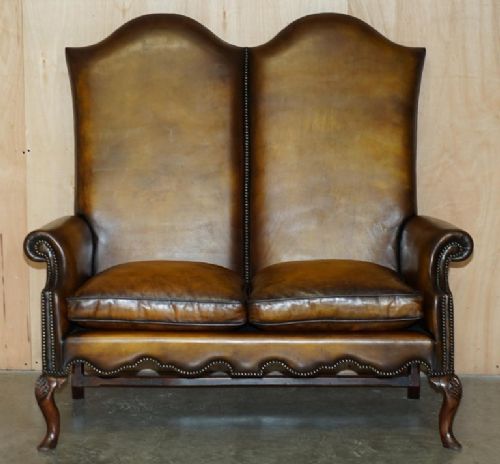 fig 1. A highback two-seater settee upholstered in warm brown leather with brass stud detailing and carved wooden cabriole legs.